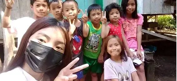 A church worker and seven smiling children outside a village home