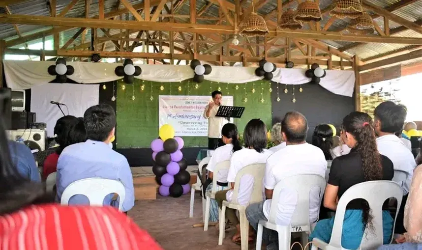 A Sunday service in progress, the congregation seated on plastic chairs under the pavilion roof