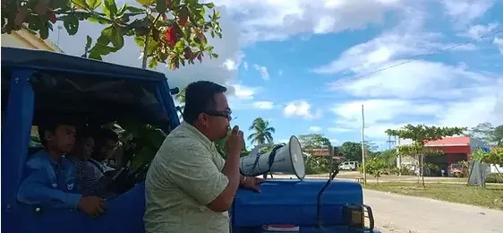 A man preaching through a megaphone from the back of a blue jeepney